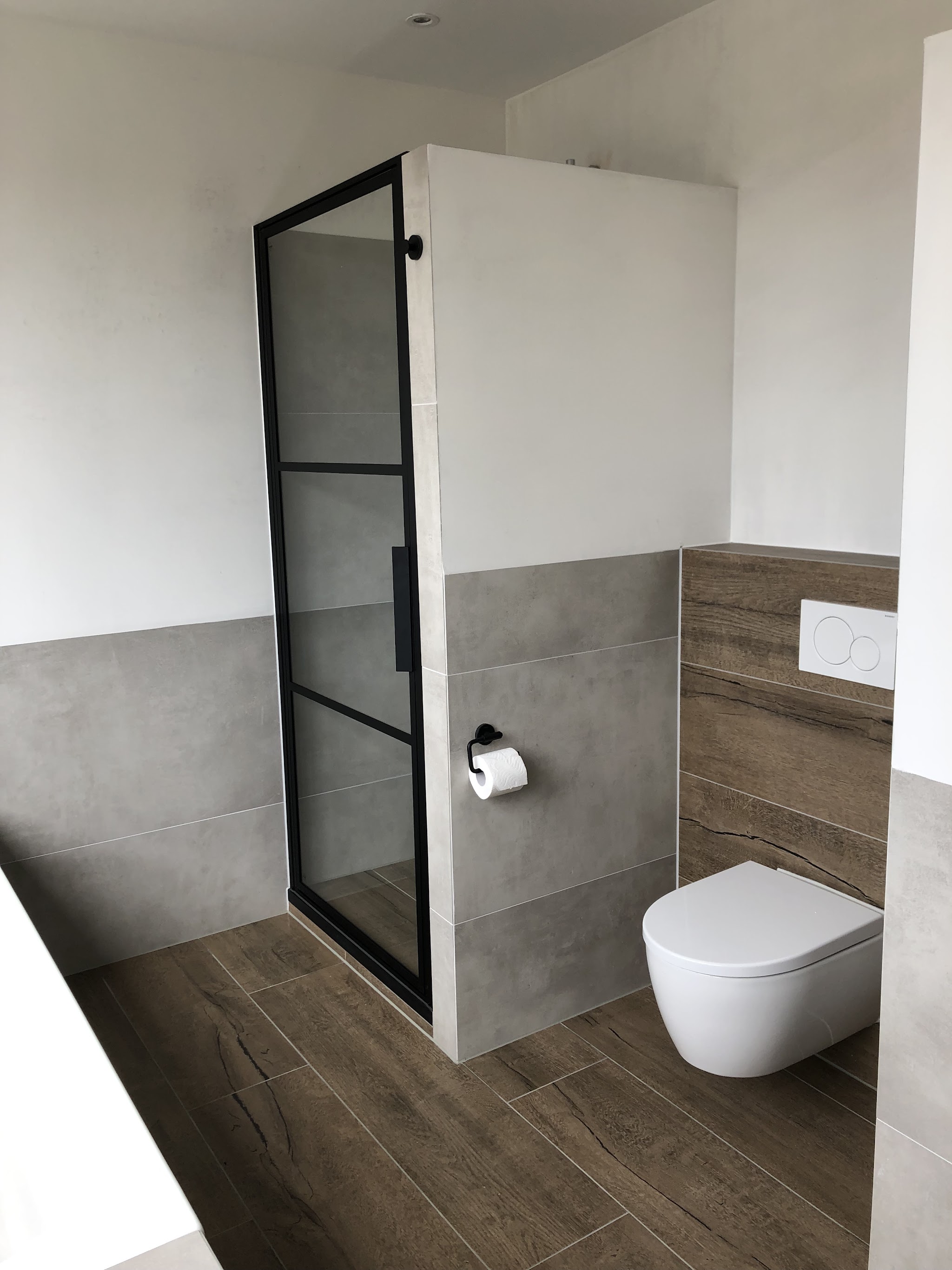 Afgewerkte badkamer met zwart stalen douchewand, hangtoilet en houtlook vloertegels