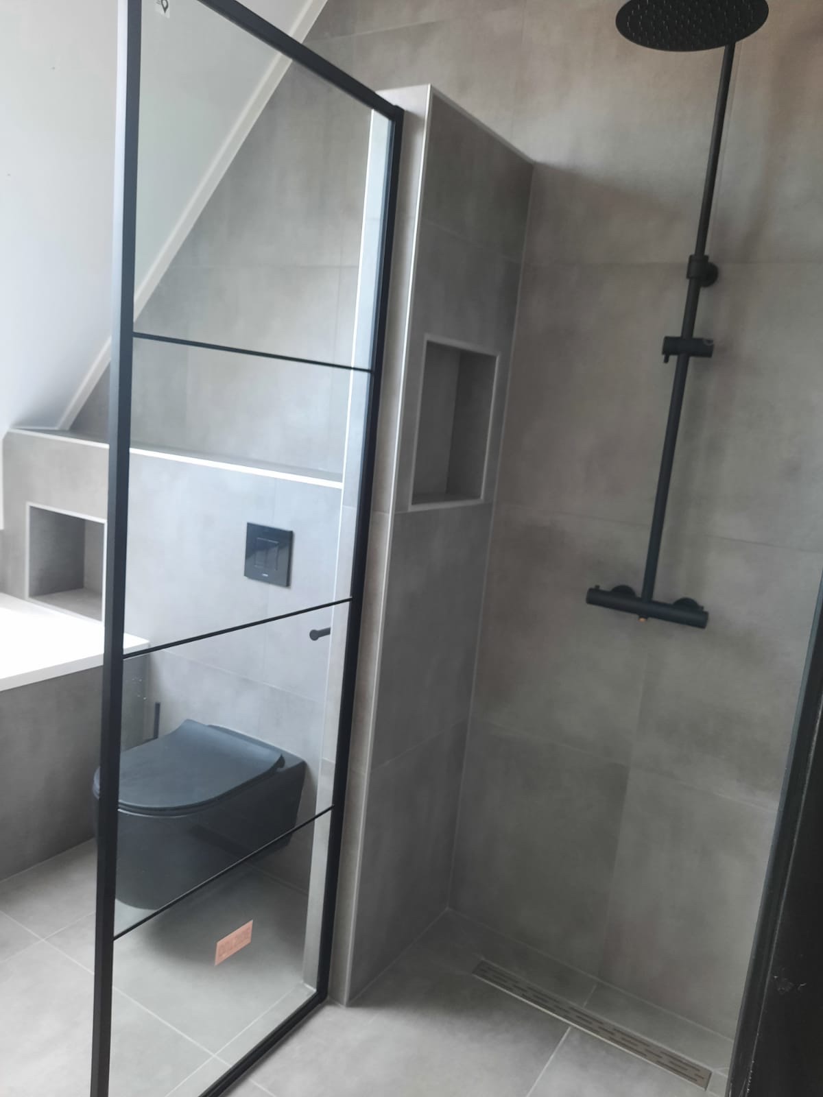 Zolderbadkamer met zwart stalen inloopdouche en nis in betonlook tegels